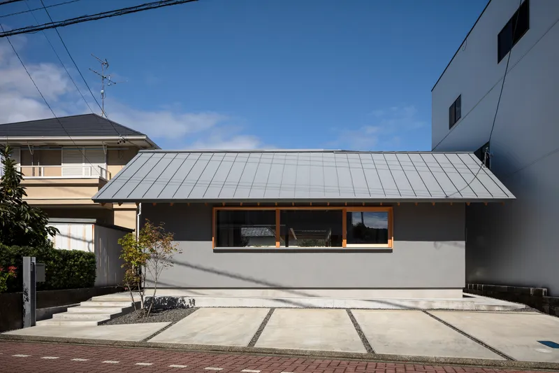 Street view of the low-pitched metal roof and horizontal timber-framed window under clear blue sky