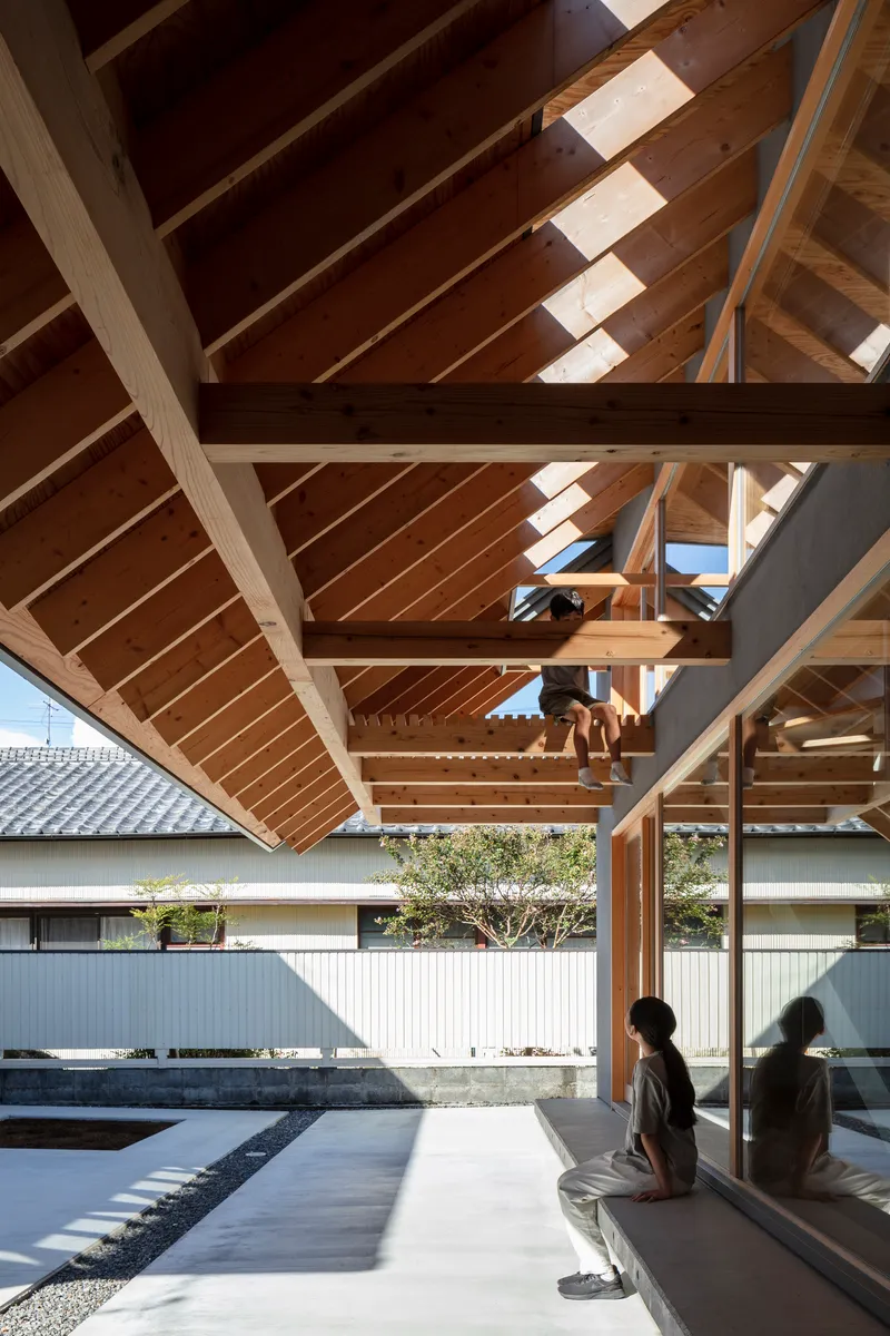Covered terrace with exposed timber frame and rafters as two figures sit overlooking the courtyard