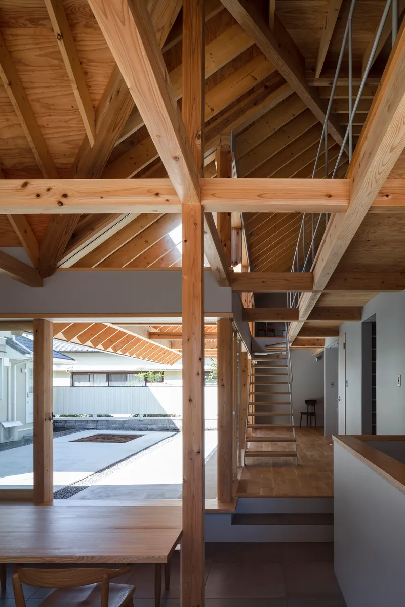 Interior living space showing timber post-and-beam structure with open staircase and view to courtyard