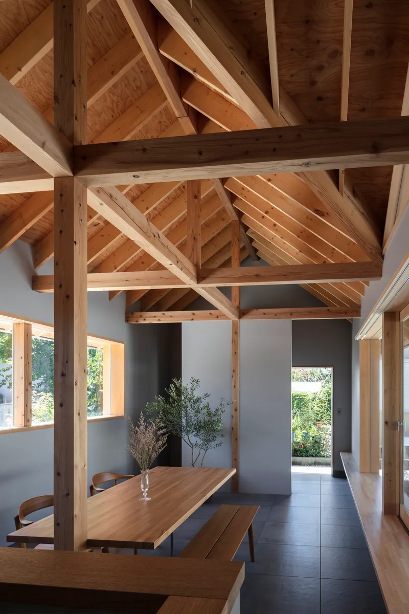 Dining area beneath exposed timber trusses with a vase of branches on the table