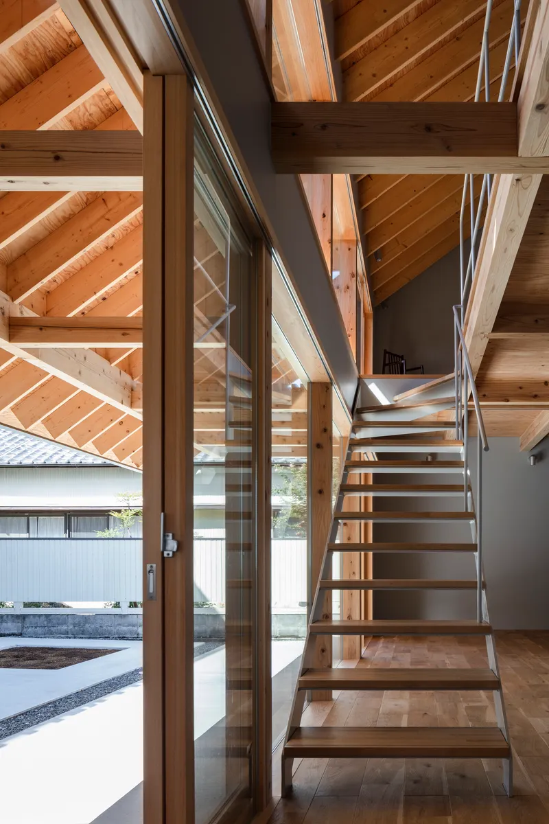 Timber staircase with steel rod railings rising through the exposed structural frame near glazed wall