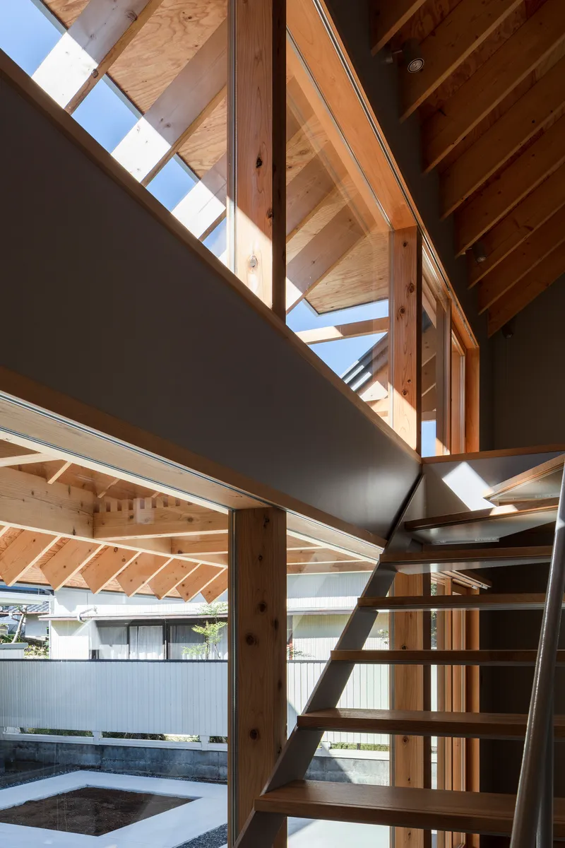 Interior view of timber staircase rising toward a skylit upper level with exposed rafters and bright afternoon sun