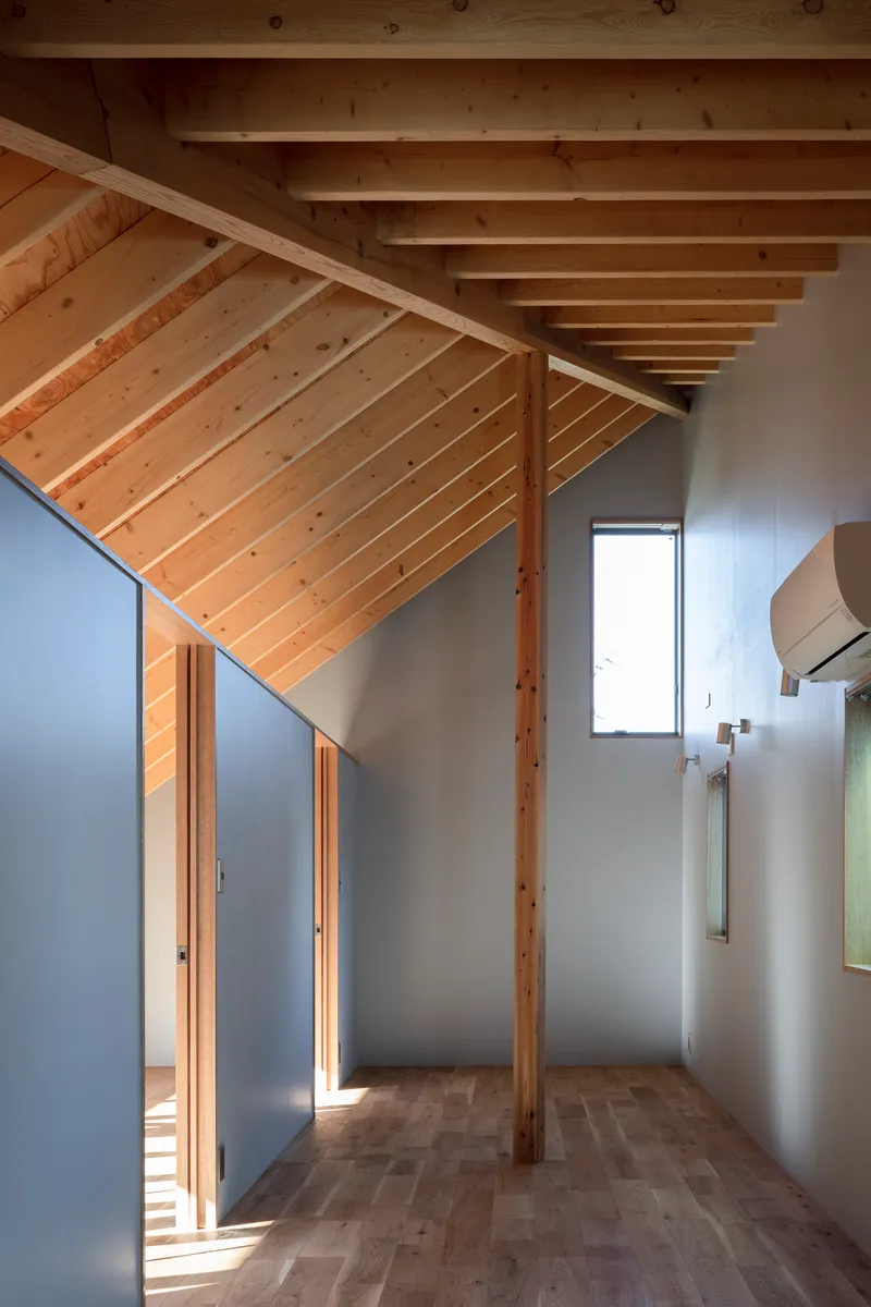 Narrow bedroom with sloped plank ceiling, timber column, grey walls and sunlight through a small window