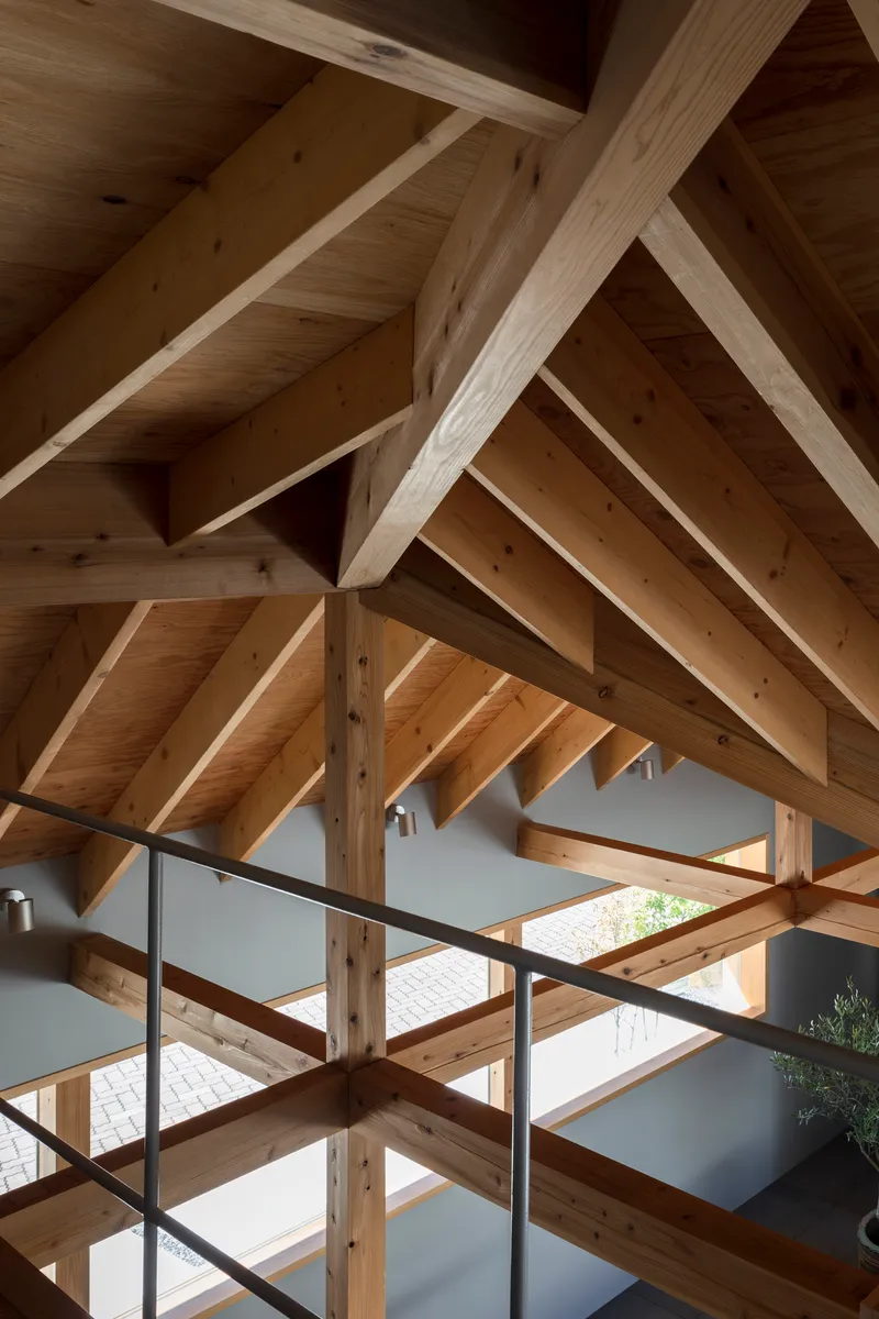 Upward view of the timber roof structure with interlocking beams and rafters above a steel railing