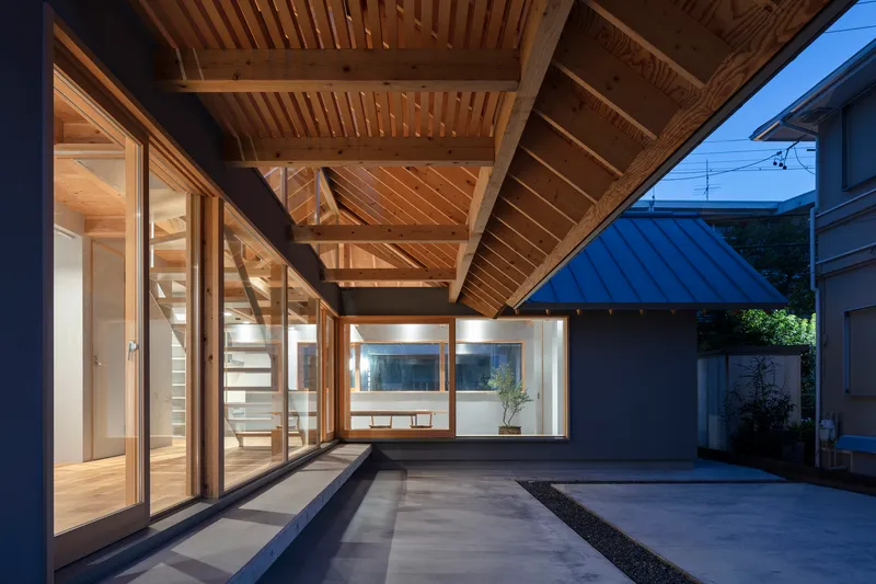 Courtyard view showing timber-framed glazing beneath a cantilevered roof with slatted ceiling at twilight
