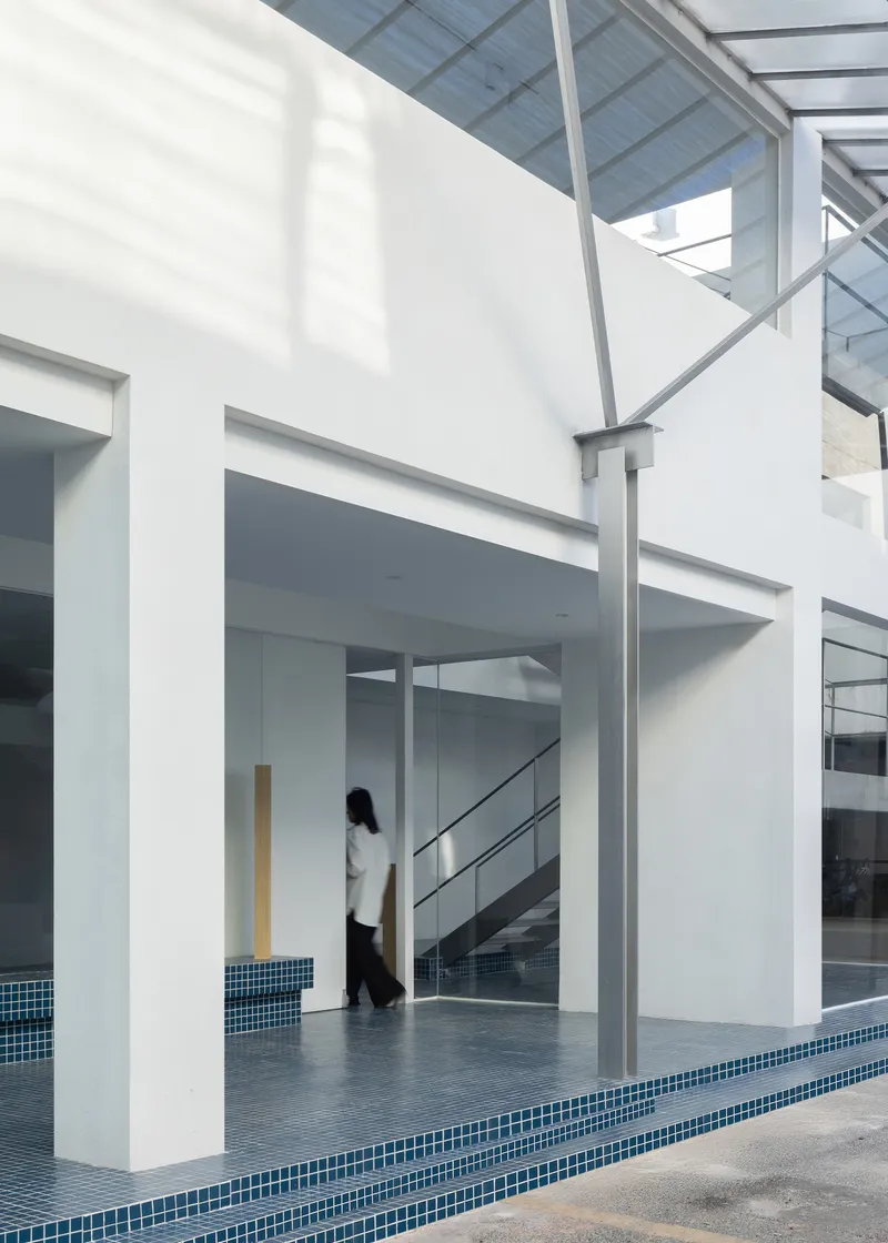 Courtyard threshold with blue mosaic tile edging and steel canopy framework overhead in daylight