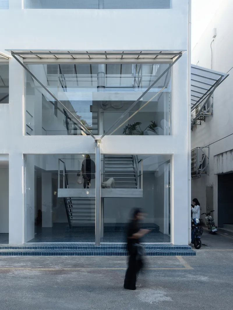 Glass facade showing three-storey interior with central staircase and figures moving in the courtyard at dusk