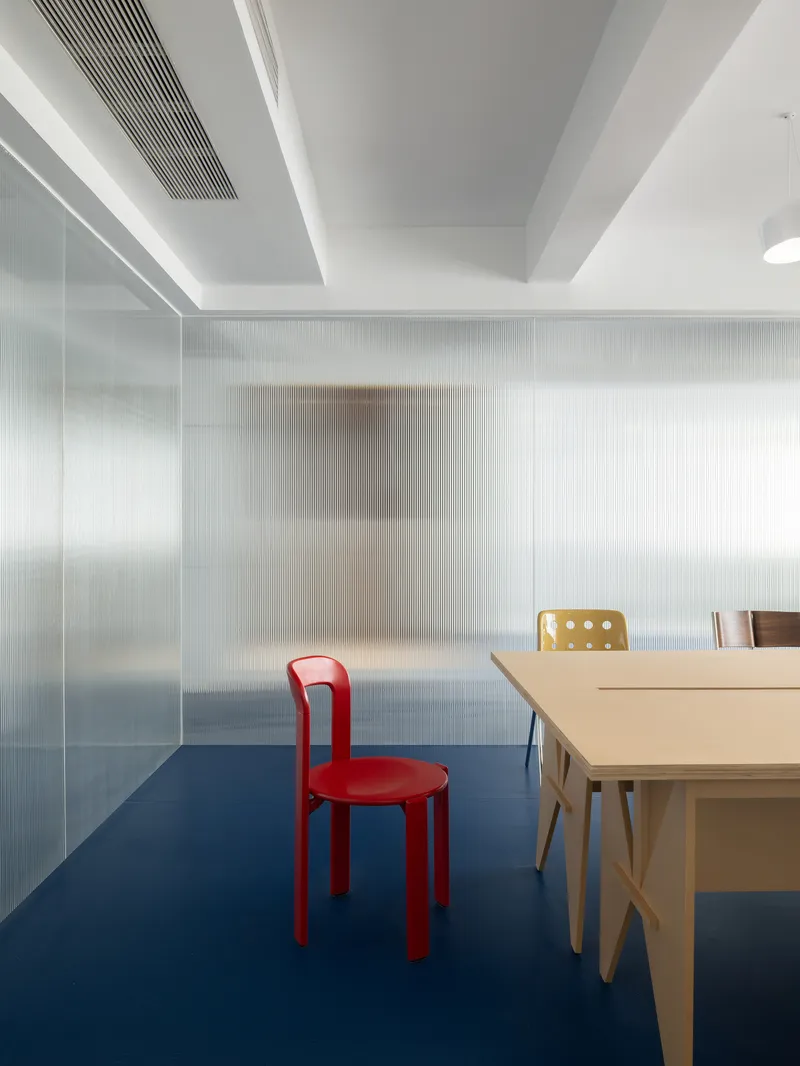 Conference room with translucent ribbed glass partitions and blue carpet beneath white pendant lights