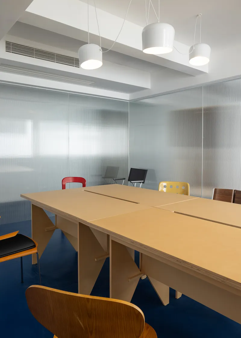 Long wooden table surrounded by mixed chairs in a room with frosted glass walls