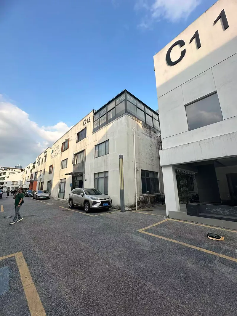 Street view of concrete facade with metal-framed rooftop addition under bright afternoon sky