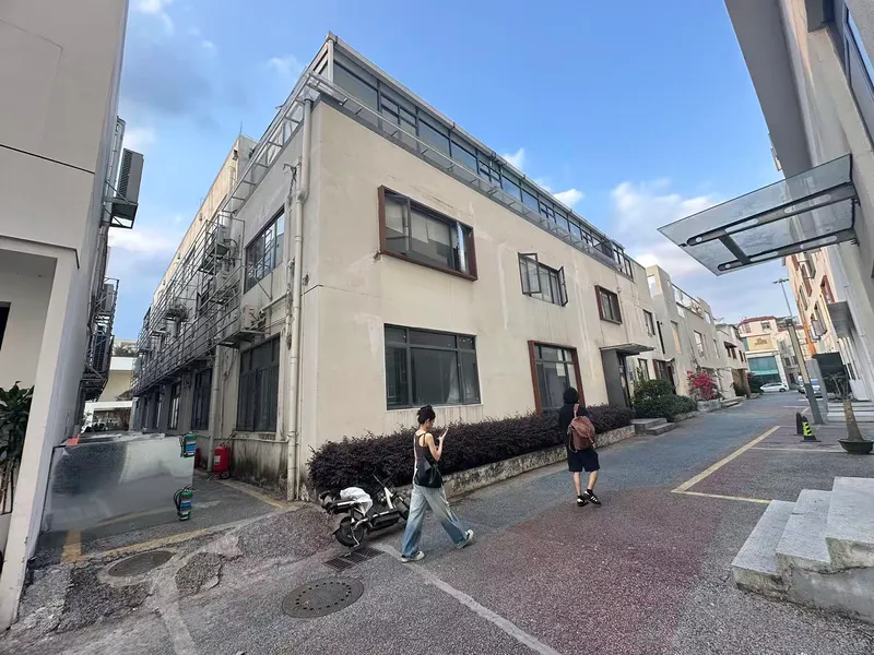 Existing warehouse building with mixed window openings as pedestrians cross the sloped roadway