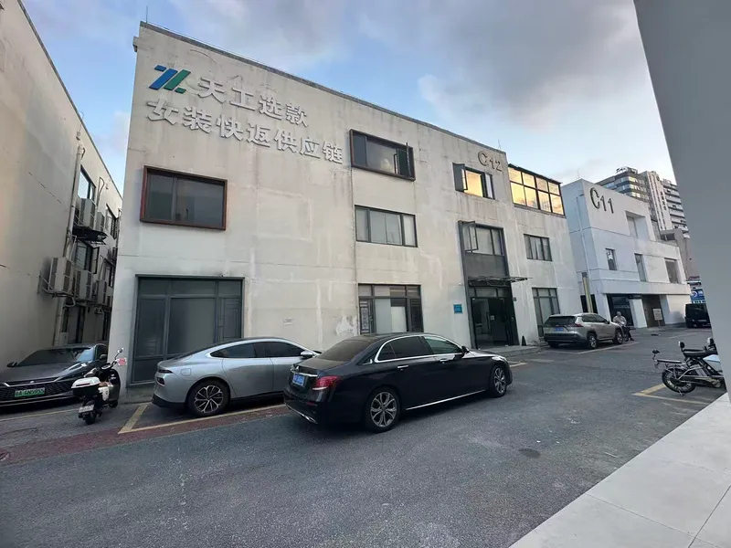 Painted concrete facade with signage facing parked cars in an industrial courtyard