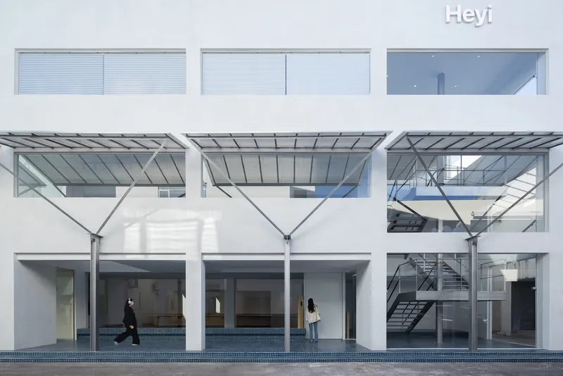 White facade with metal canopy columns and blue tile courtyard floor with two figures passing through