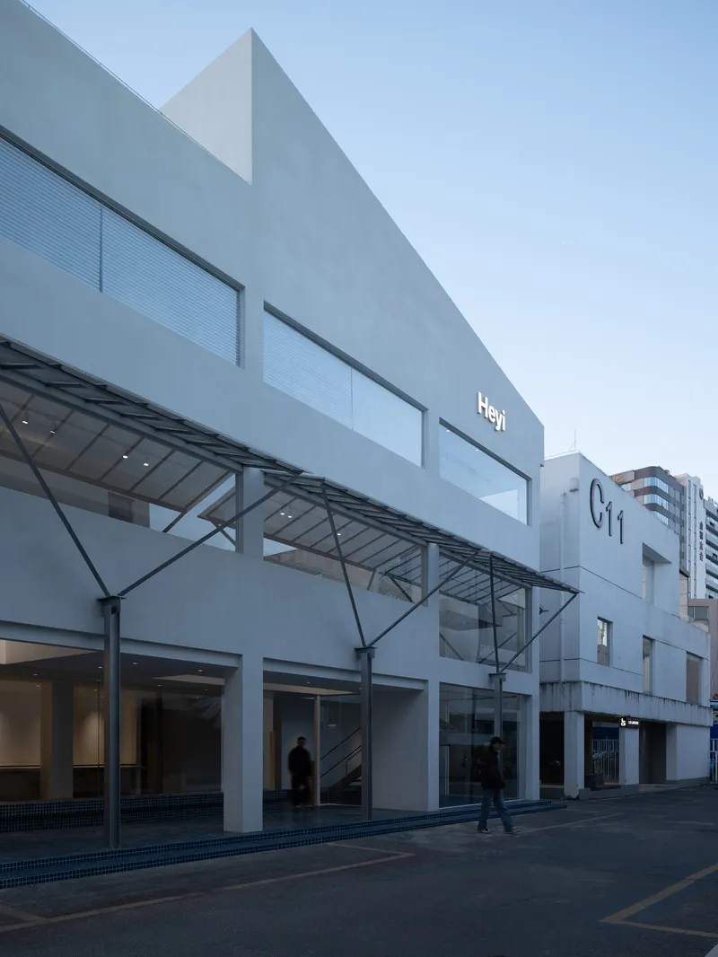 Street facade showing angled metal canopy supported by cables above a ground floor colonnade at dusk