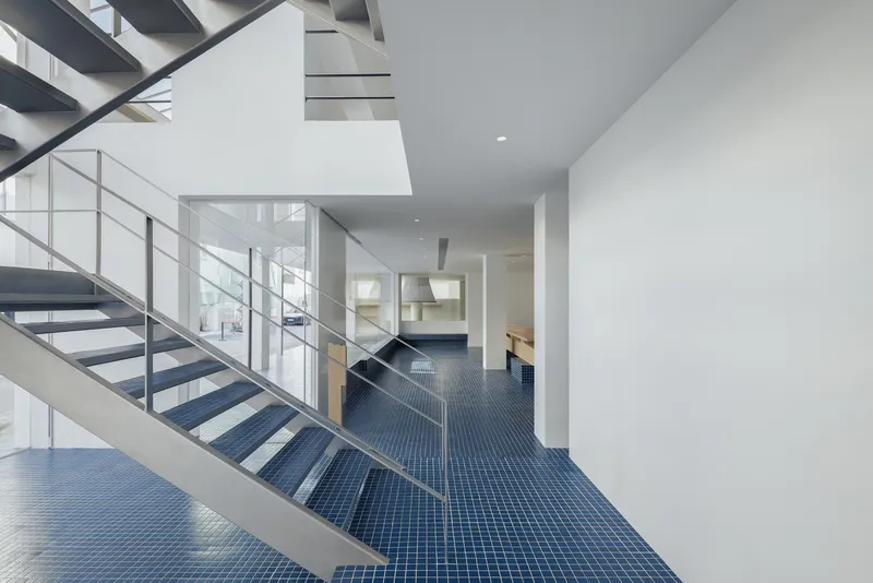 Open-tread metal staircase ascending through a white-walled space with blue tile floor and skylights above