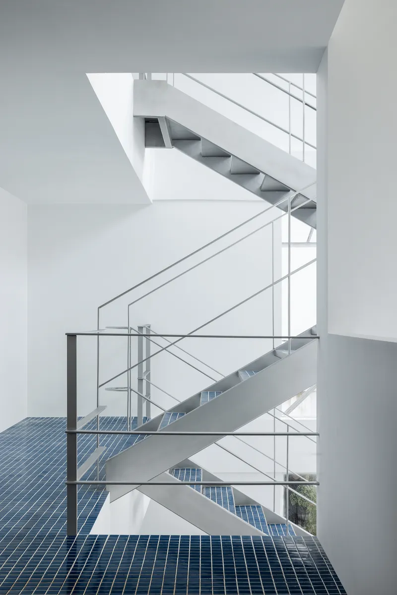 Vertical atrium view showing switchback steel staircases connecting floors with blue mosaic tile landings