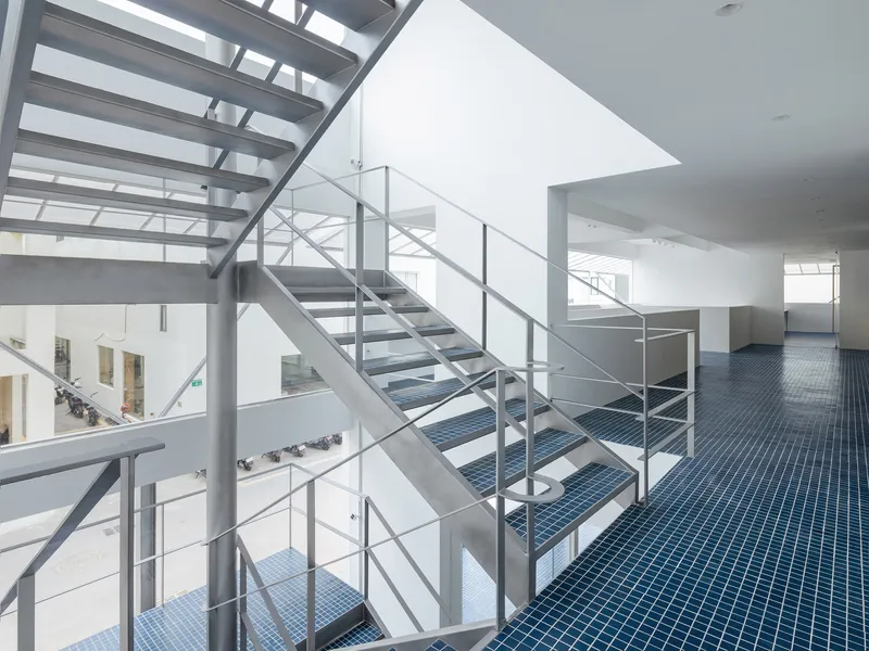 Steel staircase with open treads and wire balustrades crossing a multi-level atrium with blue tiled flooring