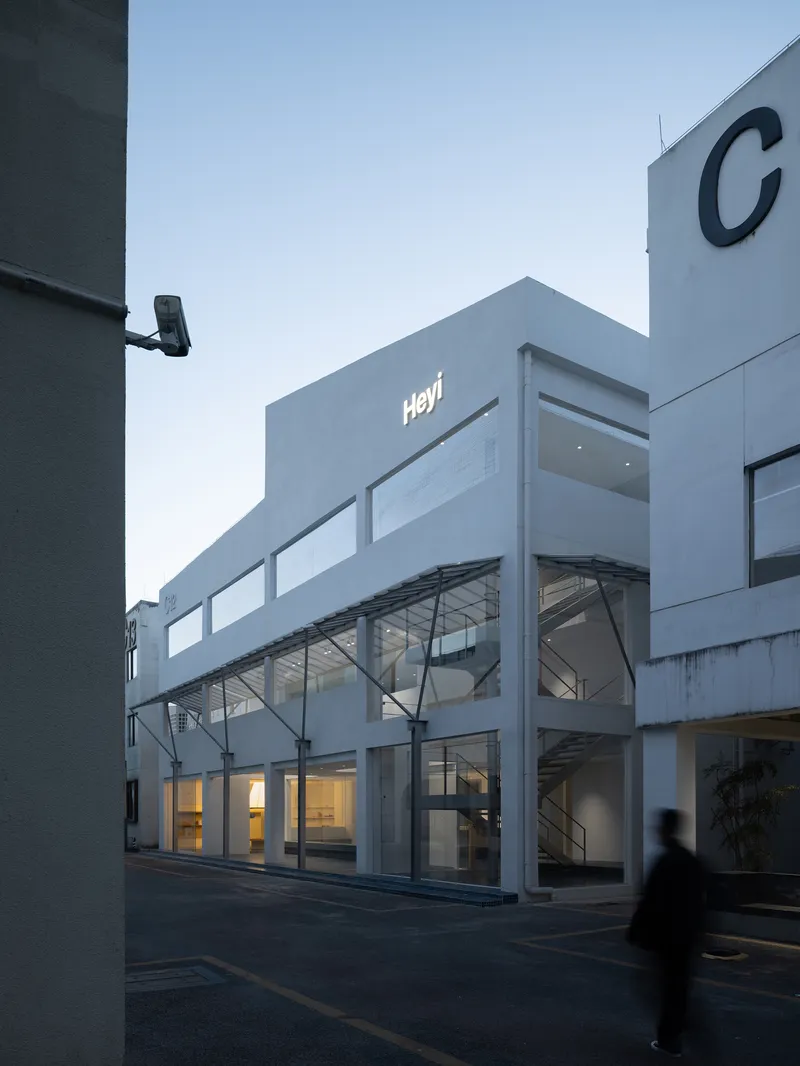 Street facade with horizontal glazing bands and diagonal steel bracing visible behind glass at dusk