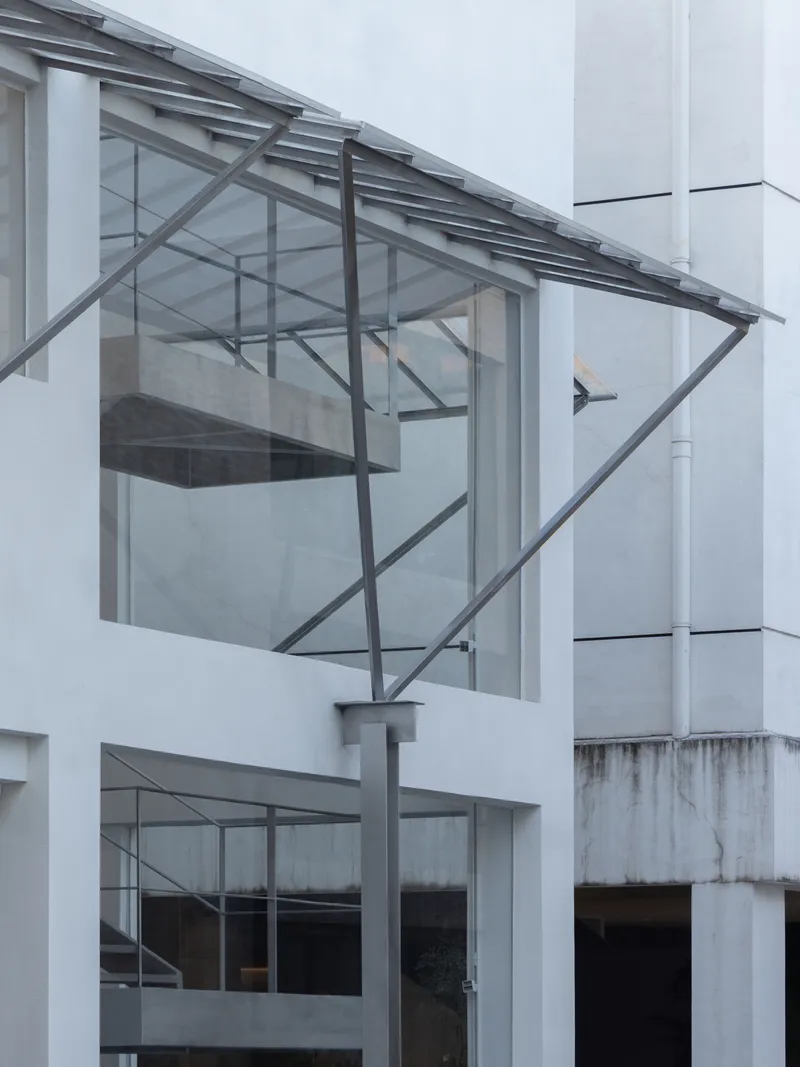 Cantilevered glass box with exposed steel frame and sloped glazed roof projecting from white facade