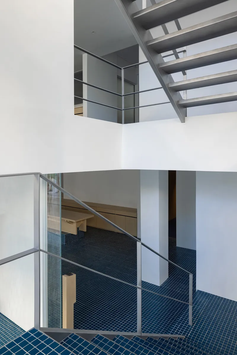 Multi-story atrium showing stacked levels with wire railings, open steel stairs, and blue diamond-pattern tile floor