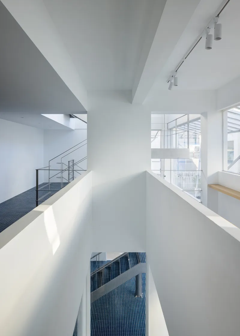 Vertical view down a white stairwell with daylight filtering through glazed openings onto blue tiled landing