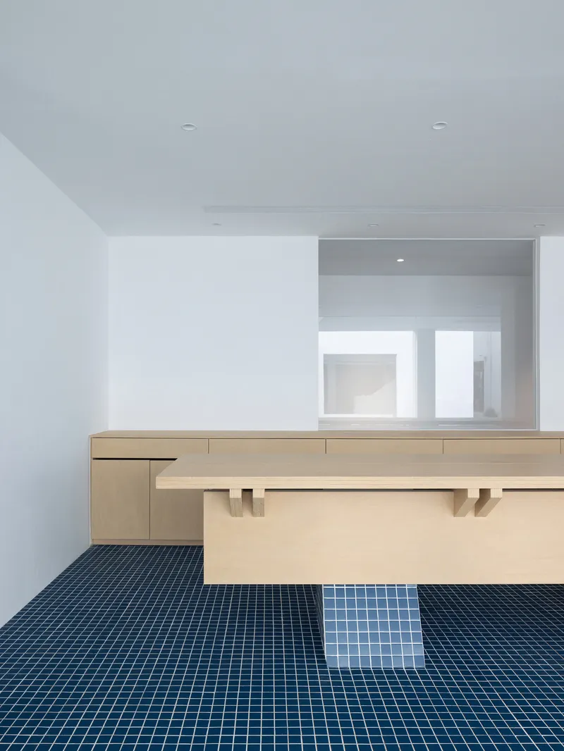 Light wood reception desk with blue mosaic tile floor and white walls under ceiling spotlights