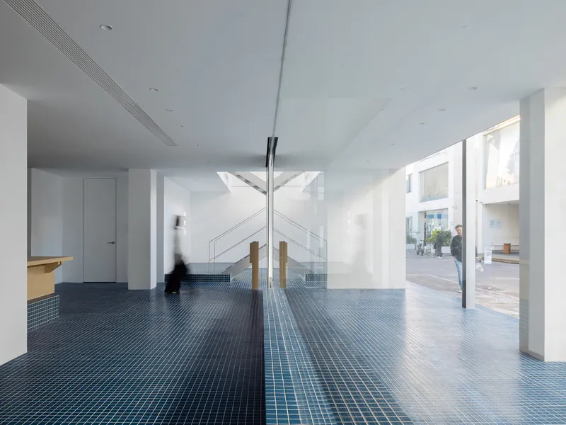 Double-height foyer with blue mosaic tile floor, timber columns, and figure passing through sunlit space