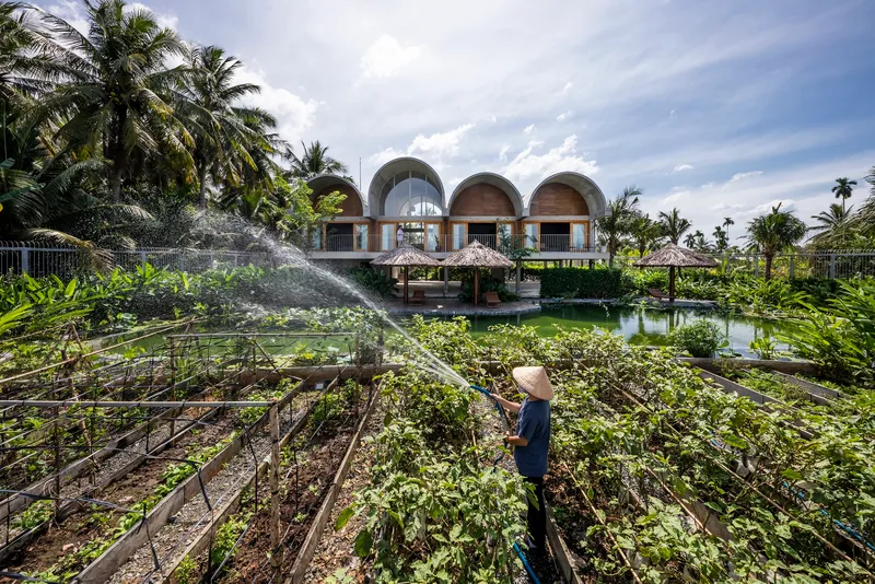 Worker tending vegetable beds with the arched roof structure and pond visible beyond