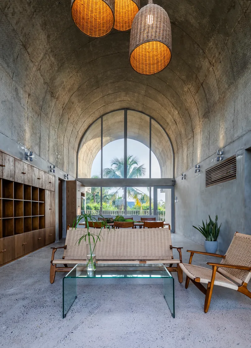 Vaulted concrete ceiling with woven pendant lights above terrazzo floor and arched window