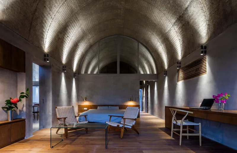 Bedroom interior showing barrel vault ceiling with uplights casting shadows on textured concrete