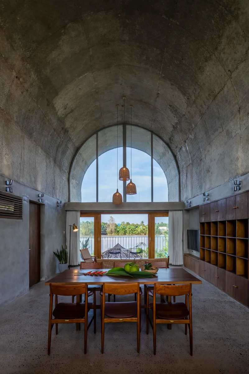 Dining area with vaulted concrete ceiling and arched window framing a view of the water beyond