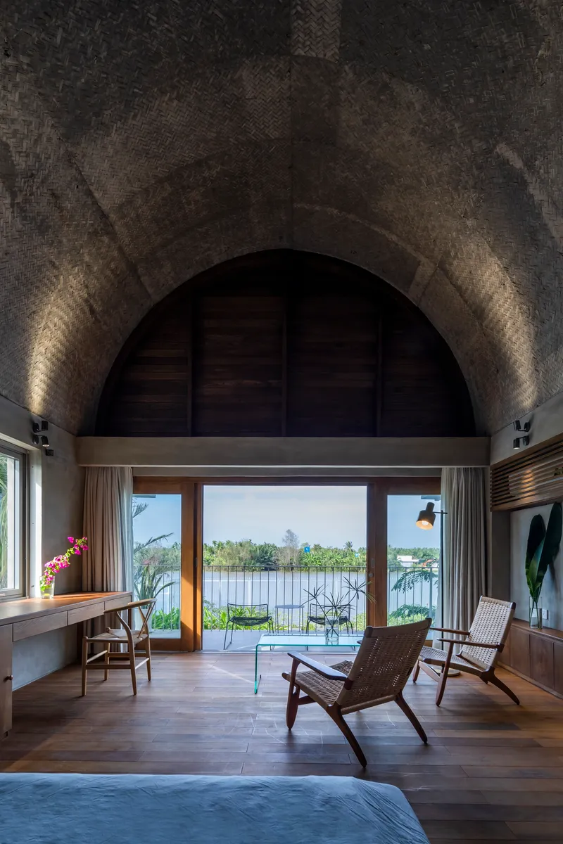 Interior view through arched opening with woven chairs beneath a vault illuminated by uplights