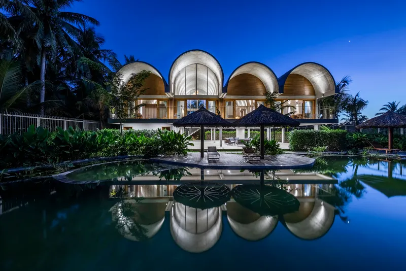 Four barrel vaults reflected in the swimming pool at dusk with palm trees silhouetted behind