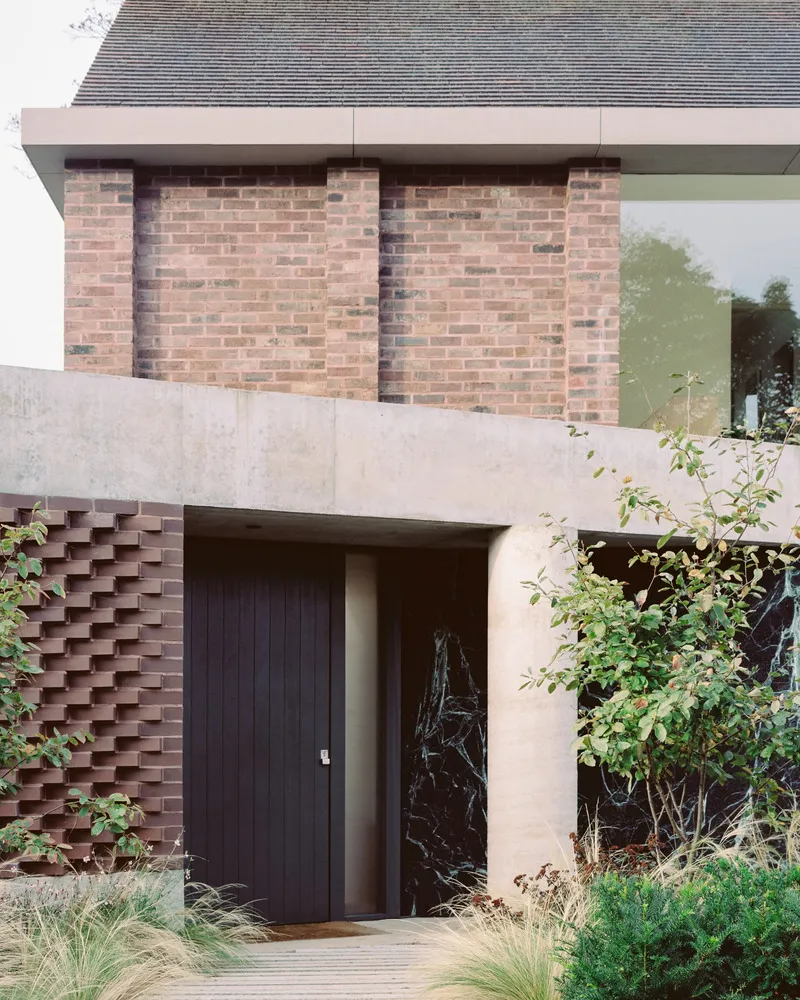 Street entry showing black timber door set within concrete portal and staggered brick screen wall