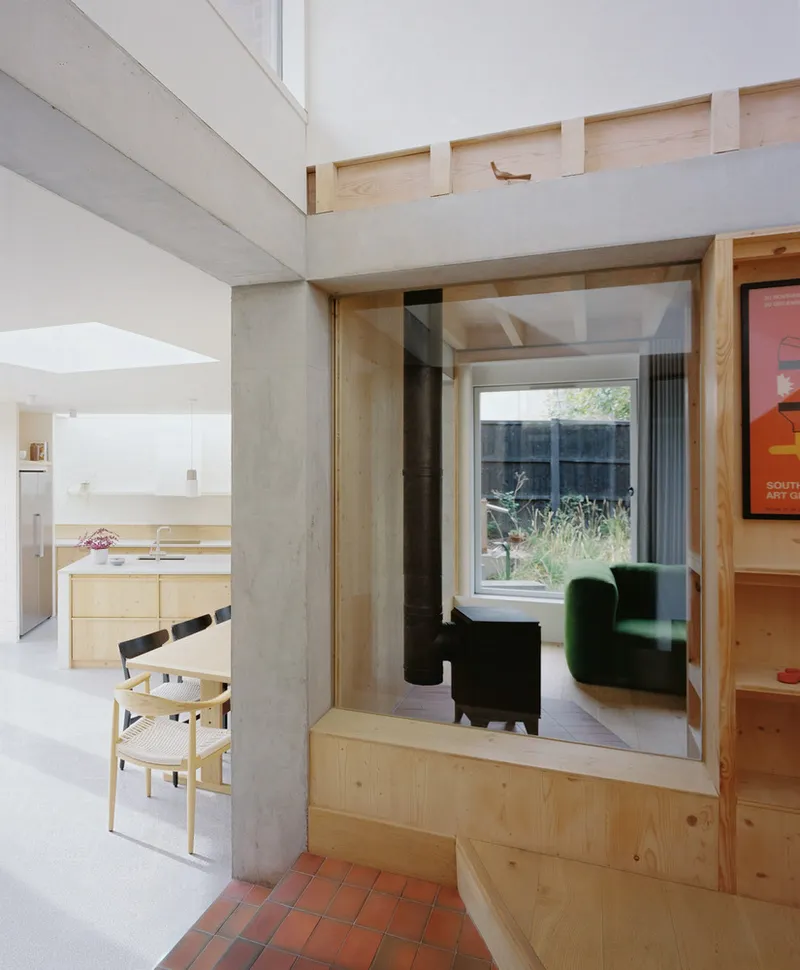 Interior view through a pine-framed glazed aperture connecting terracotta-paved entry to living room beyond