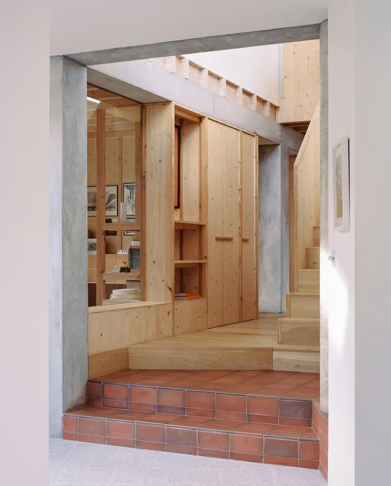 Entry hall with terracotta tile steps leading up to timber built-in storage and staircase