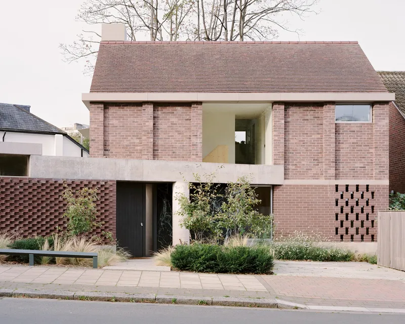 Street view of the pink brick facade with chequered brickwork panels and front garden plantings