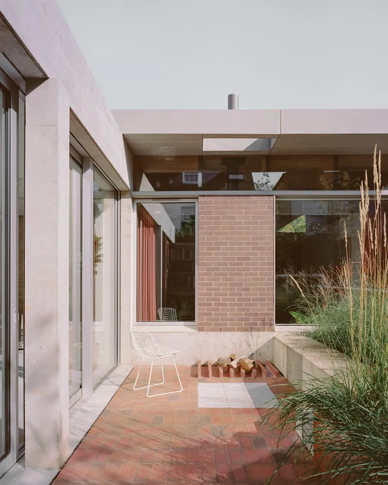 Terracotta-paved courtyard framed by pink brick walls and planted grasses in afternoon light