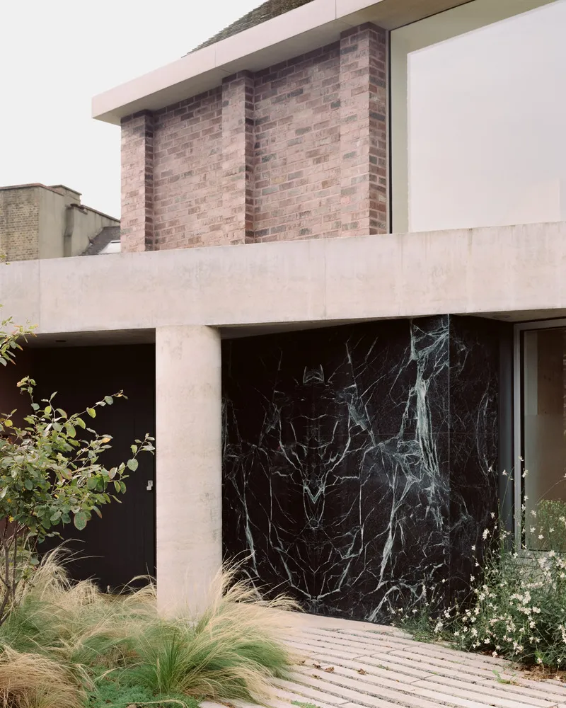 Close-up of black veined marble panel behind concrete frame and planted garden bed