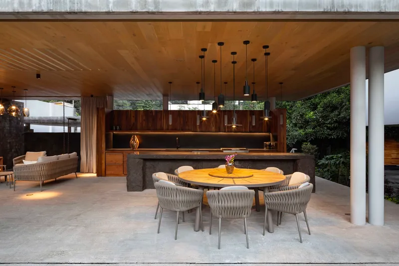Open dining and kitchen pavilion with a round table, pendant lights and a timber ceiling