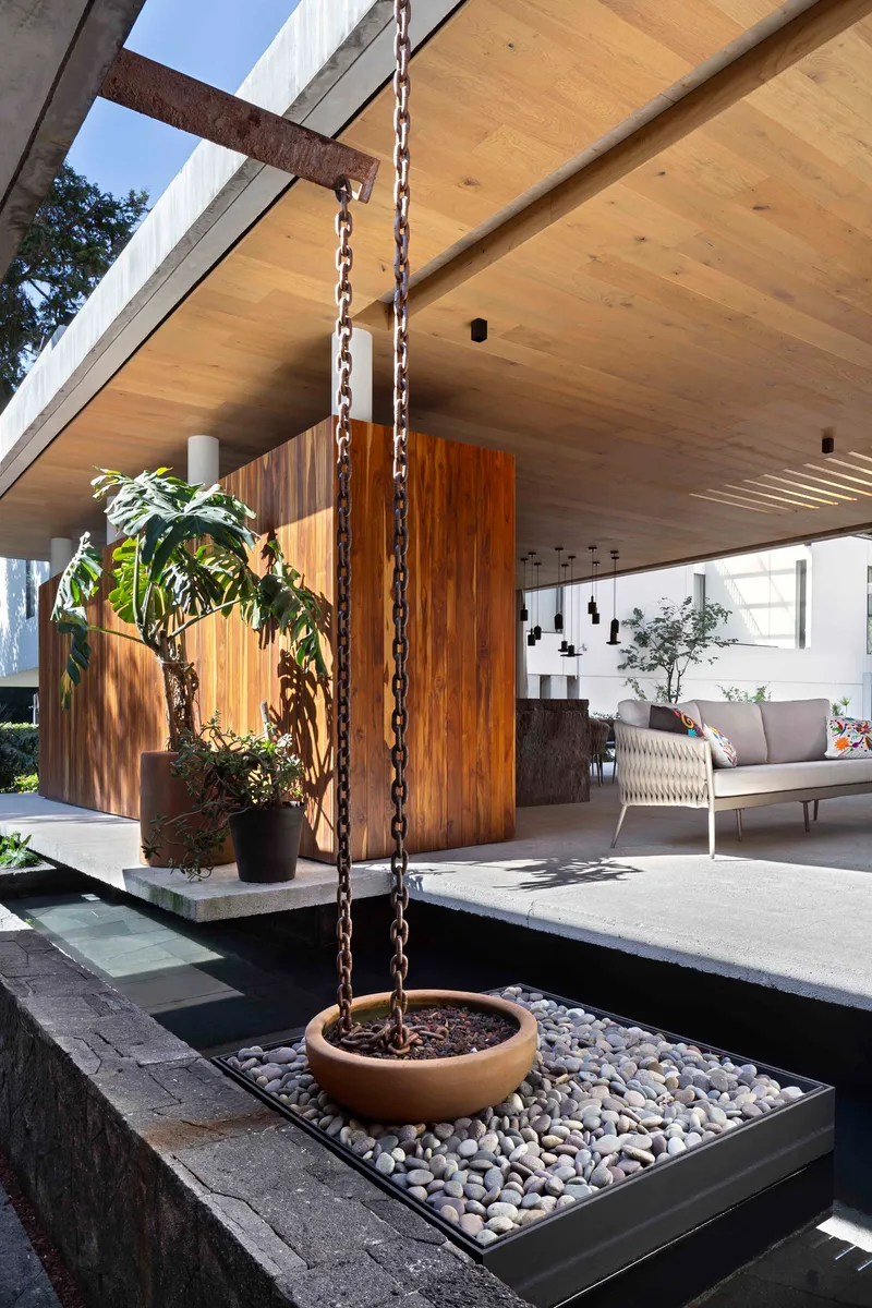 Hanging planter on chains beside the timber-clad pavilion volume above a pebble bed