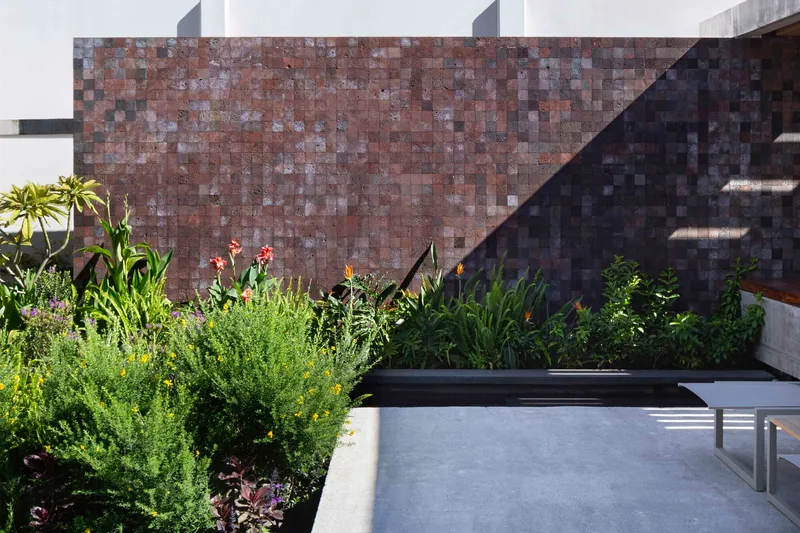 Red volcanic stone tile wall behind a planted bed with bird-of-paradise and grasses