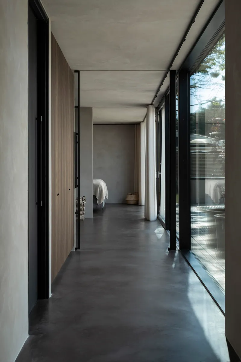 Corridor with polished concrete floor flanked by floor-to-ceiling glazing and timber-clad walls