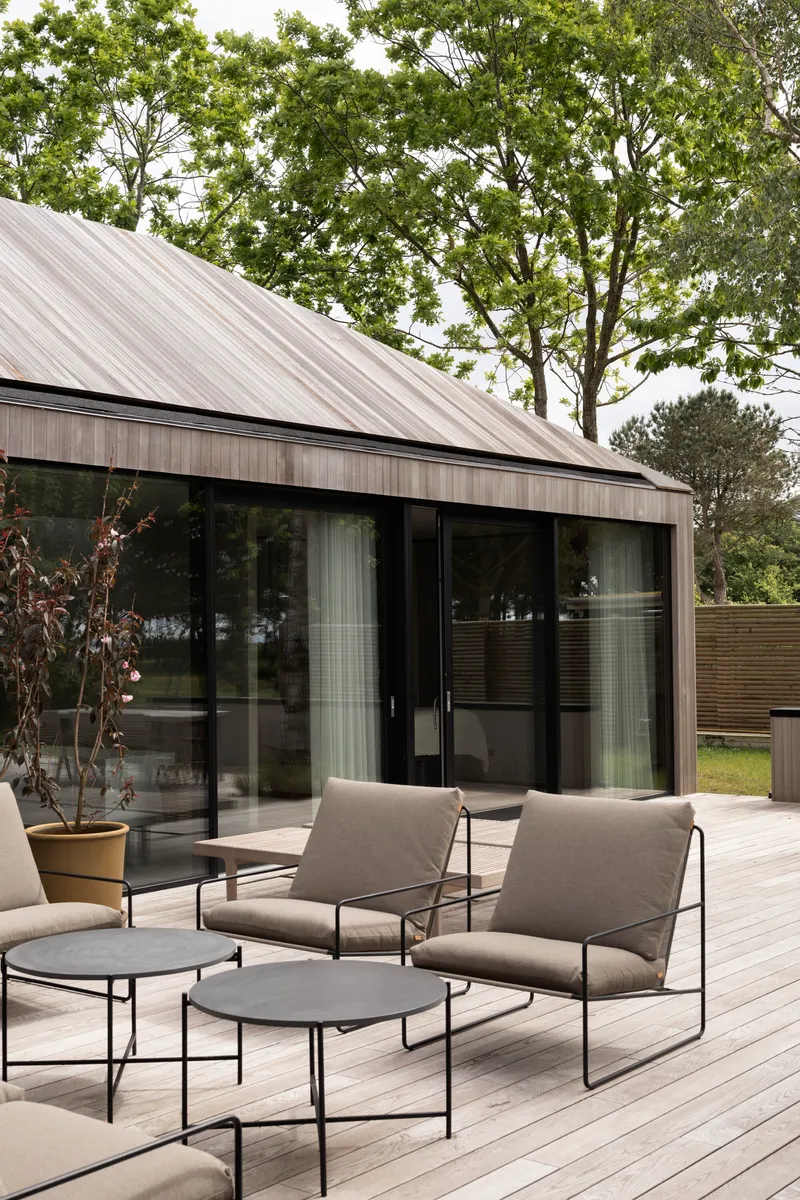 Timber deck with metal-framed seating beneath a sloped metal roof and surrounding deciduous trees