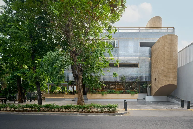 Street view showing translucent glass block facade and cylindrical buff brick tower framed by mature trees