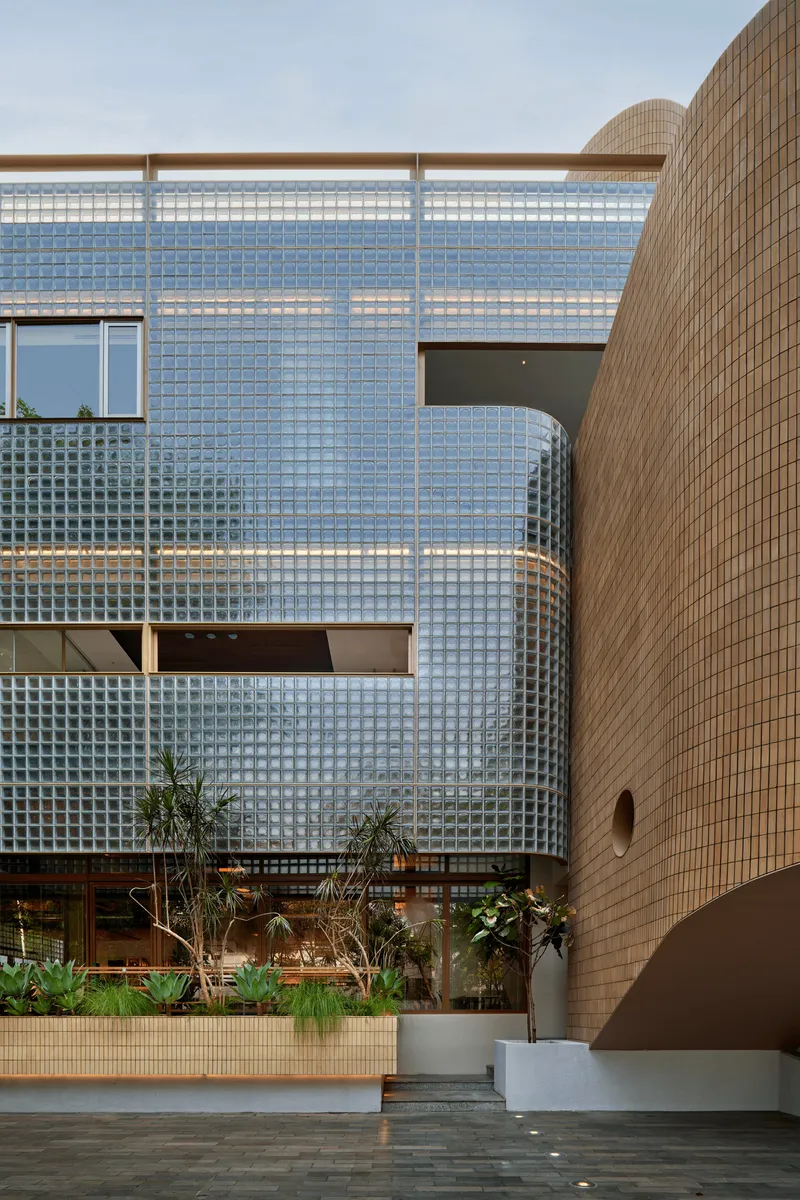Glass block wall with rectangular openings beside cylindrical brick tower and ground level planted beds