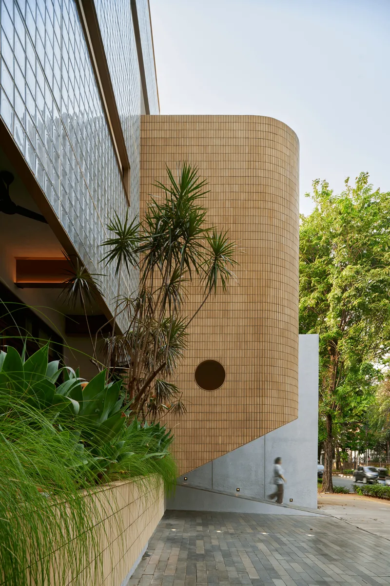 Cylindrical brick tower with circular window opening and figure passing along white base wall