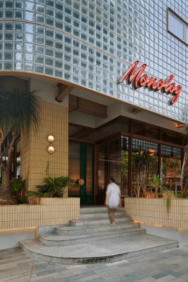 Entrance steps leading to glazed doors beneath a glass block facade with a figure walking