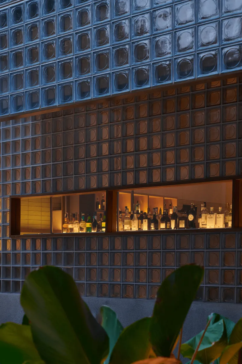 Glass block facade with horizontal bar opening revealing backlit bottles at dusk