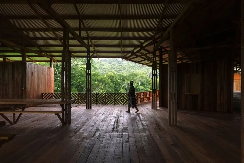 Interior walkway with exposed timber beams and columns as a figure walks toward the forest view